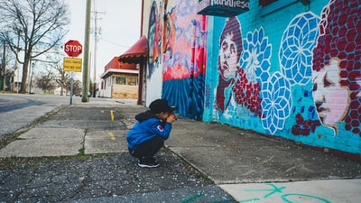男孩穿蓝色连帽衫与艺术品在墙前面
